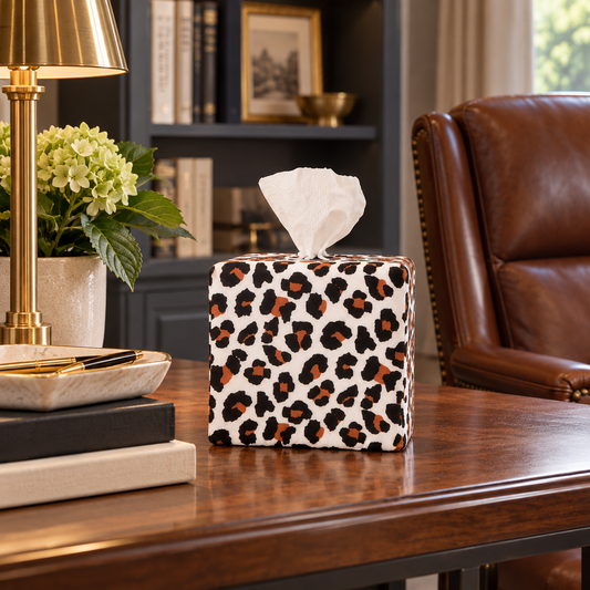 An AchooBox with Modern Leopard cover sits on a dark wood table in a styled home office setting with a leather chair, lamp, and books.