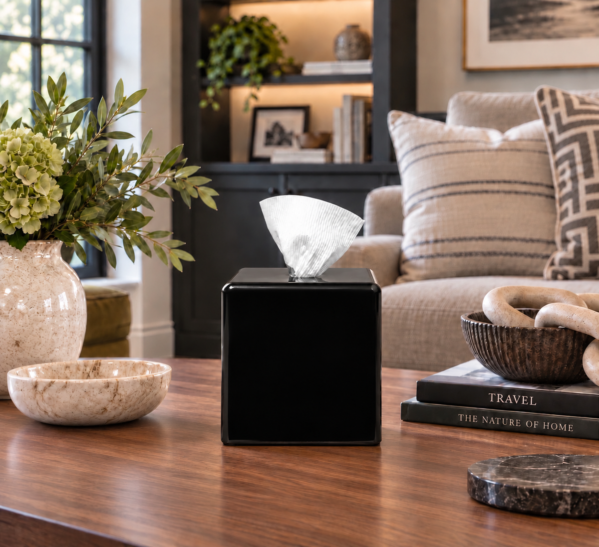 A black AcBhooox conceals your favorite bath tissue, dispensing it smoothly out the top. Soft rounded edges and smooth finish, styled on a wooden table in a modern living room setting.