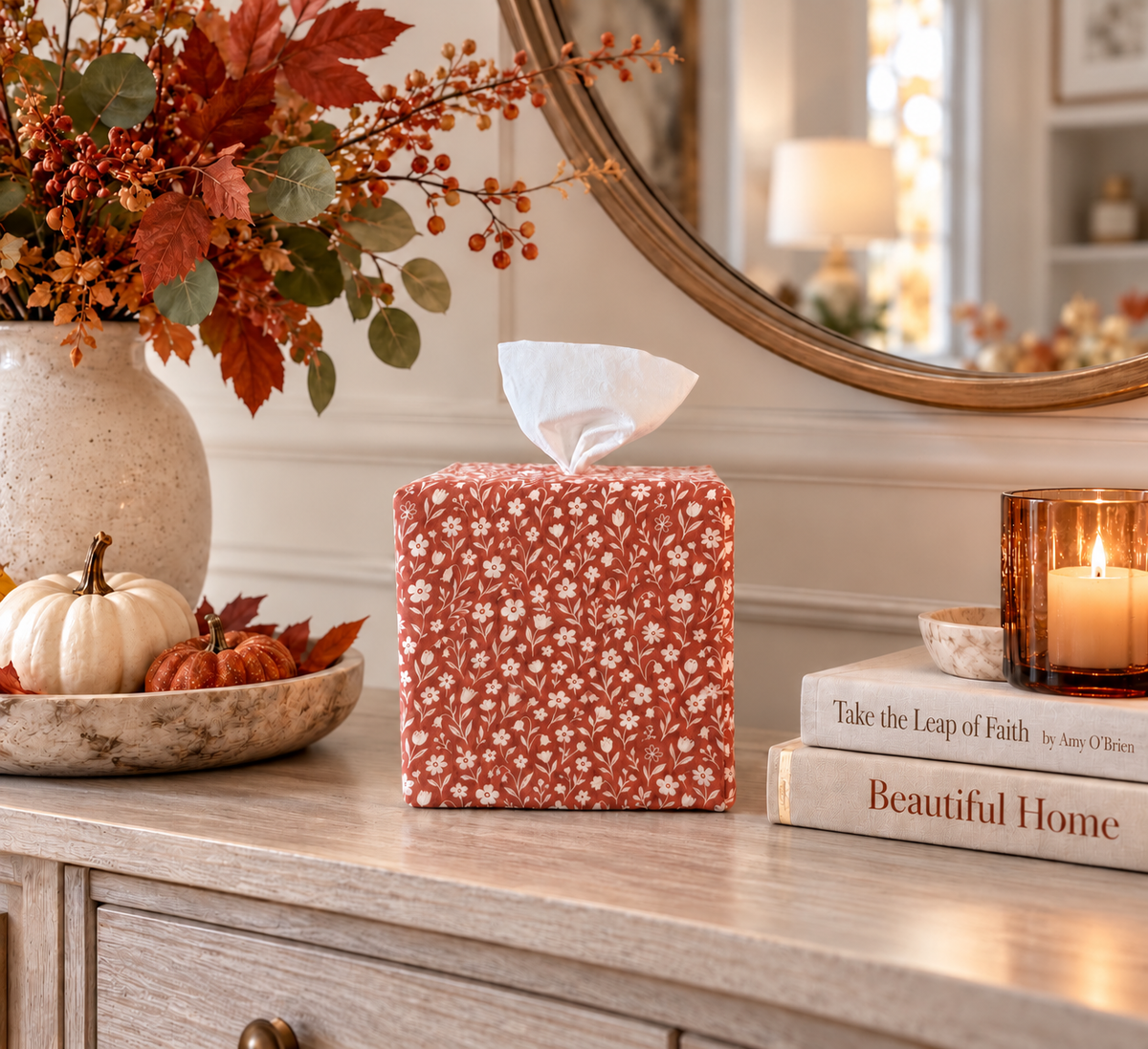 Rooibos Tea Bloom AchooBox Rolled Tissue Dispenser on autumn inspired console table next to a bowl of pumpkin gourds and books with candle on top. 