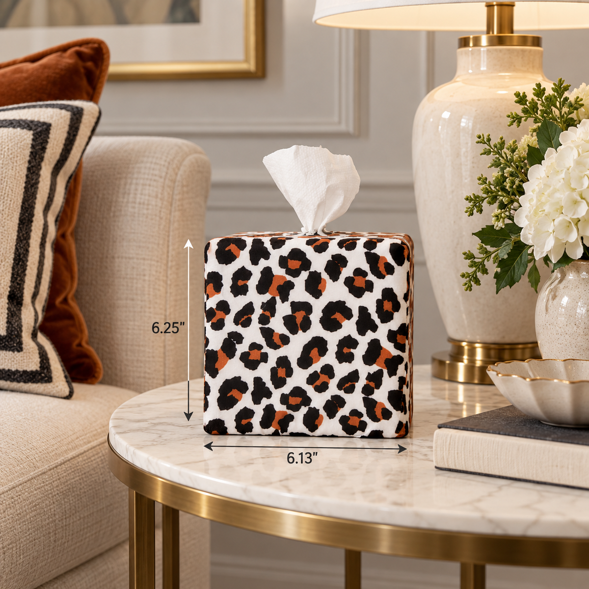 AchooBox in Modern Leopard has a white, and rust-brown leopard print pattern. It sits on a marble-top table in a styled living room. Black dimension arrows and text indicate 6.13" wide by 6.25" tall.