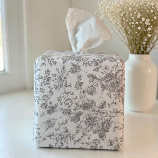 Parisian Slate Heirloom Toile AchooBox with bath tissue concealed inside and coming out of the top like a standard tissue box. White vase with baby's breath in the background.
