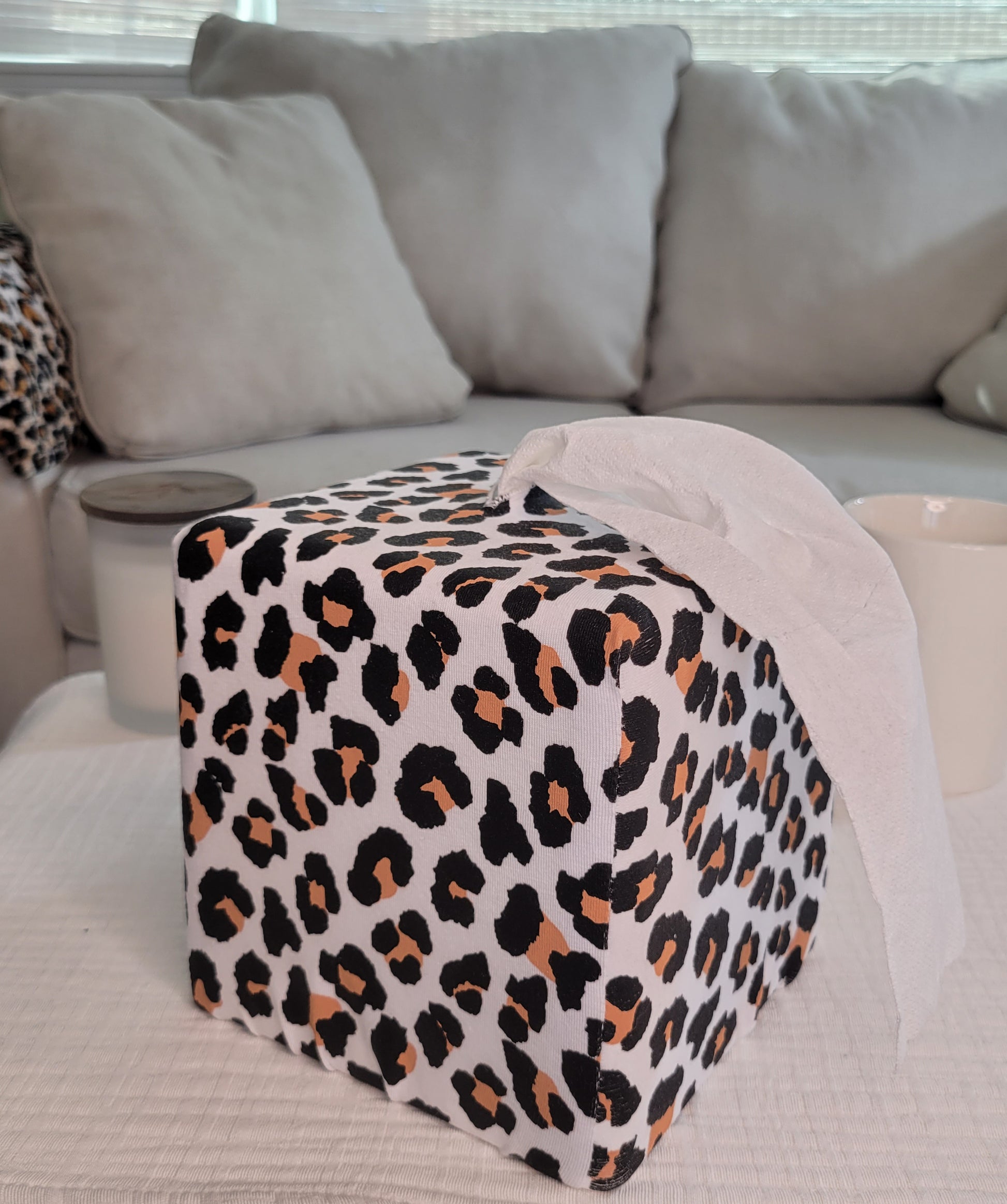 Modern Leopard printed AchooBox Rolled Tissue Dispenser on coffee table with long tail of bath tissue dispensed from the top